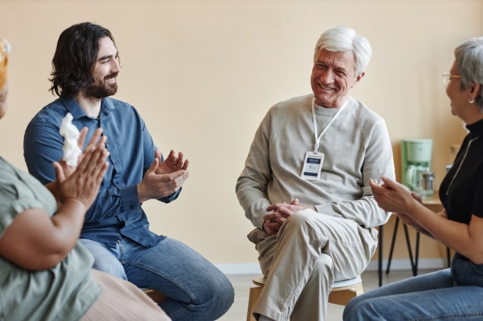 Group of smiling people applauding to man sitting in circle at support group and sharing success stories